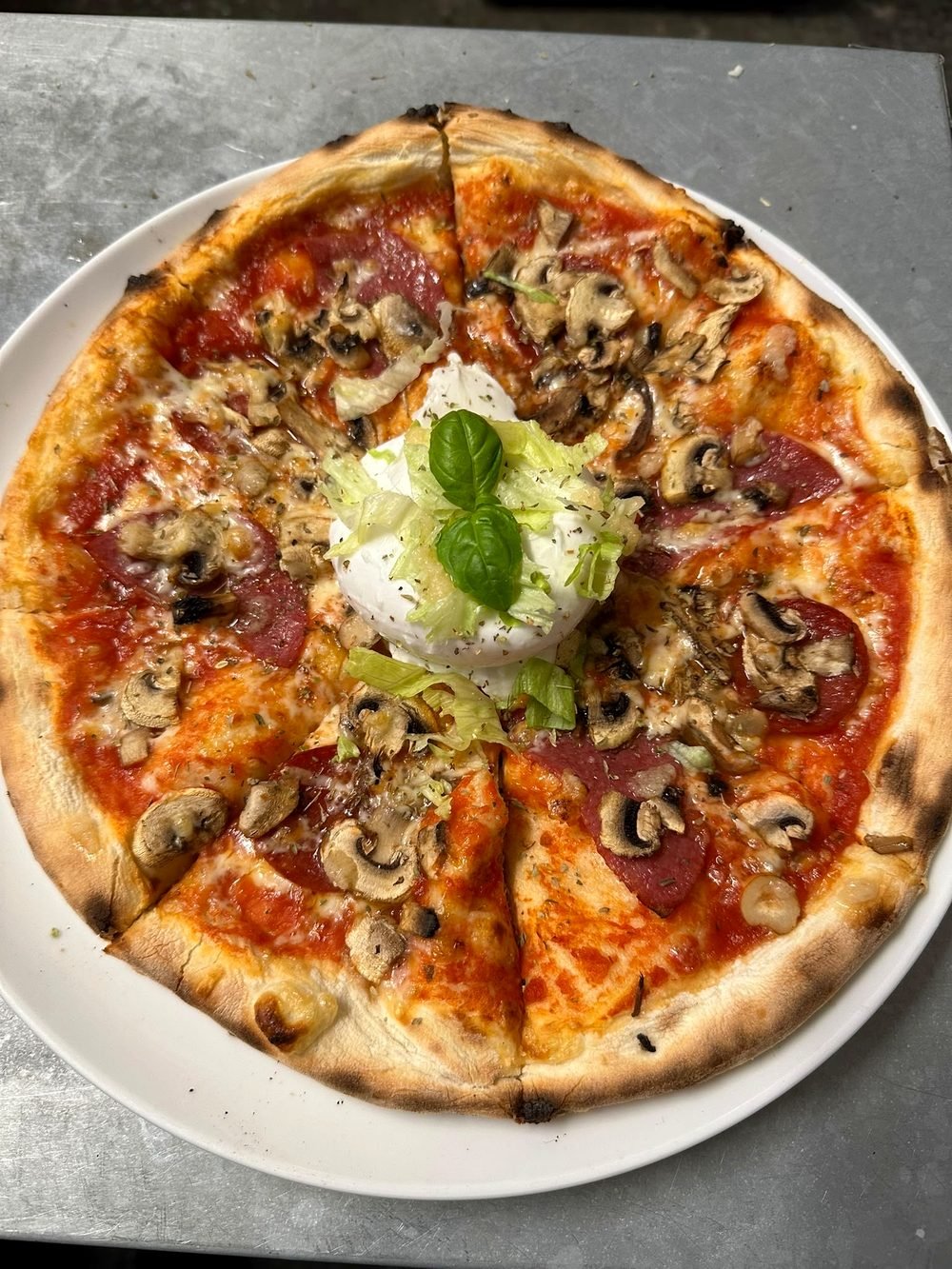 Pizza mit Champignons, Salami und einer Kugel Mozzarella in der Mitte