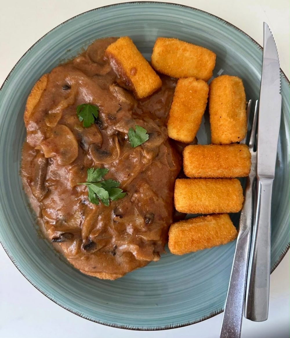 Schnitzel mit cremiger Sauce und Kroketten auf einem Teller