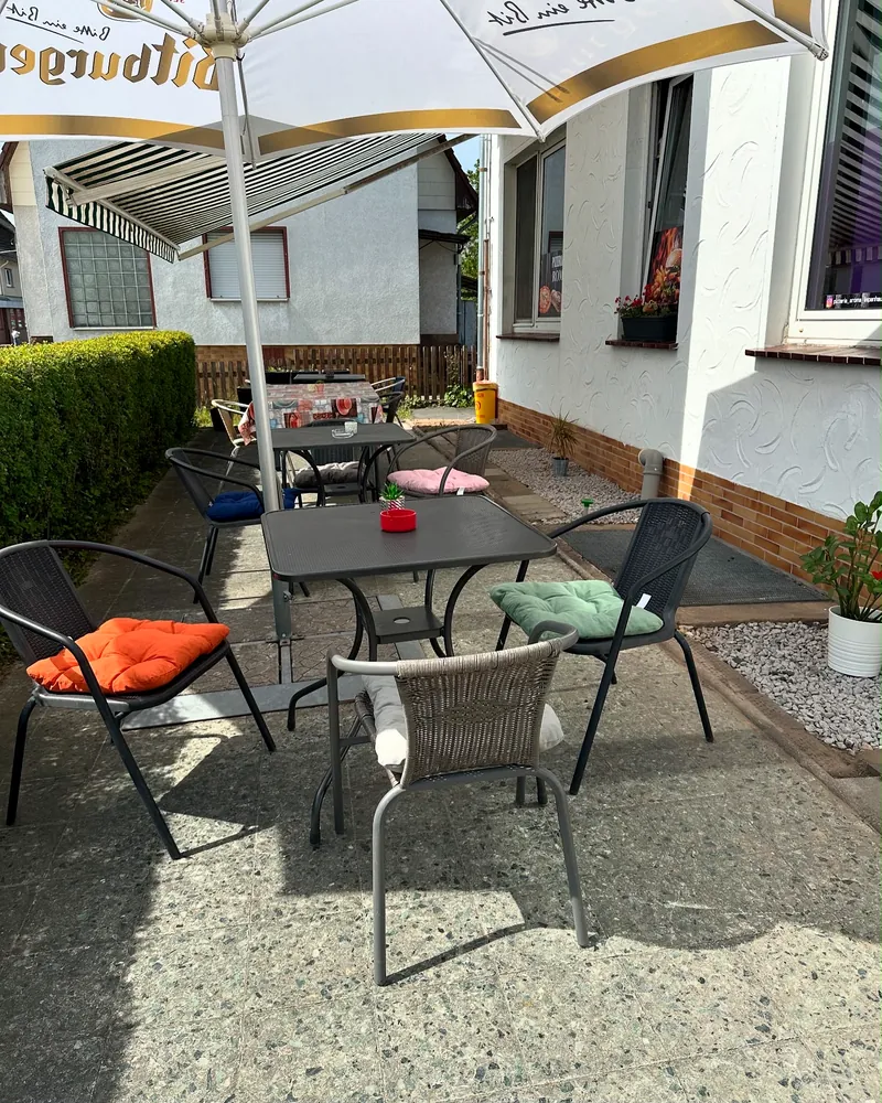 Sonniger Außenbereich mit Tischen, Stühlen und Sonnenschirm